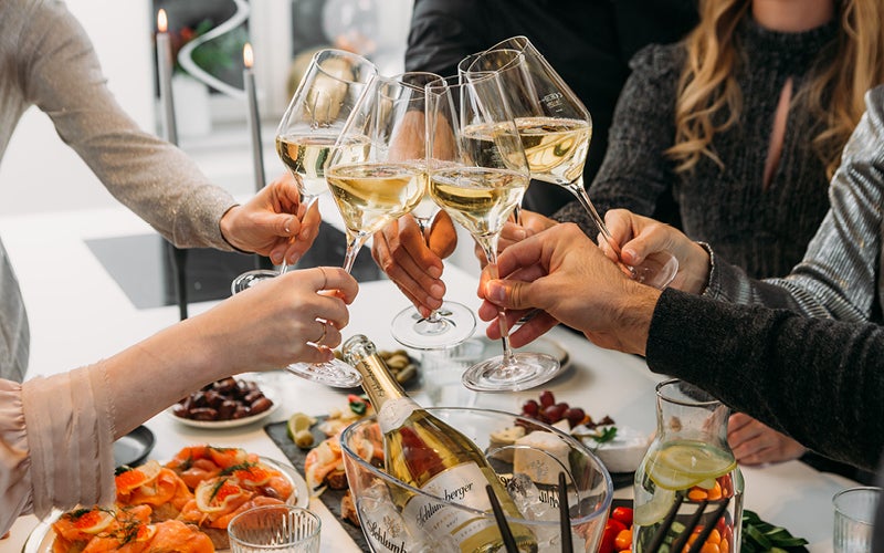 Grote tafel met eten waar veel handen proosten met gevulde glazen wijn
