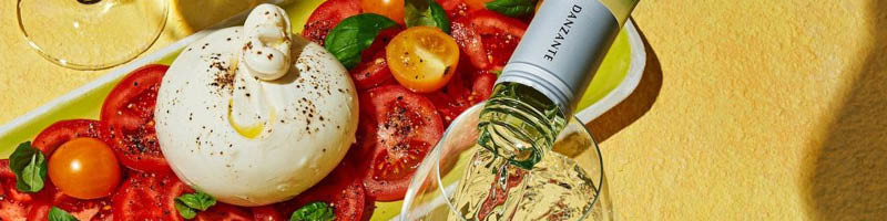 Tafel met tomaten en burrata op een bord waar witte wijn wordt ingeschonken
