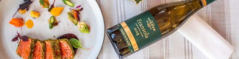 Welke wijn bij zalm Bord met zalm en groenten op tafel met een fles Fransola witte wijn